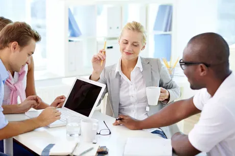 Woman with cup of coffee smiling, and a man working with co-workers behind a laptop